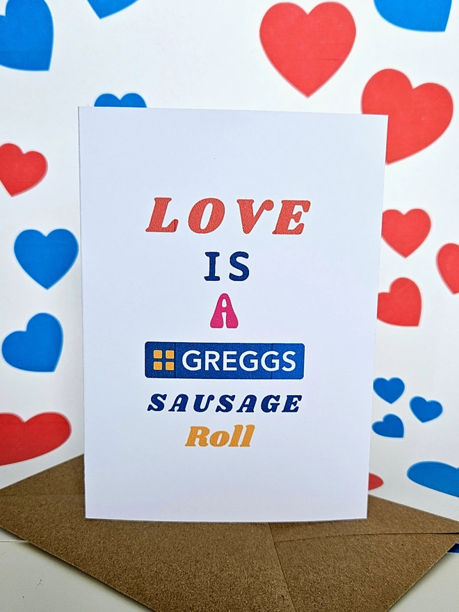 A photograph of the front of a humorous A6 greeting card illustrated using brightly coloured text. The text says love is a Greggs sausage roll