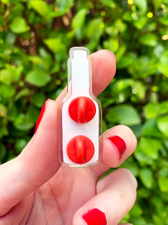 image shows the back of an acrylic badge shaped like a bottle. the back has two red rubber clutches sticking out.