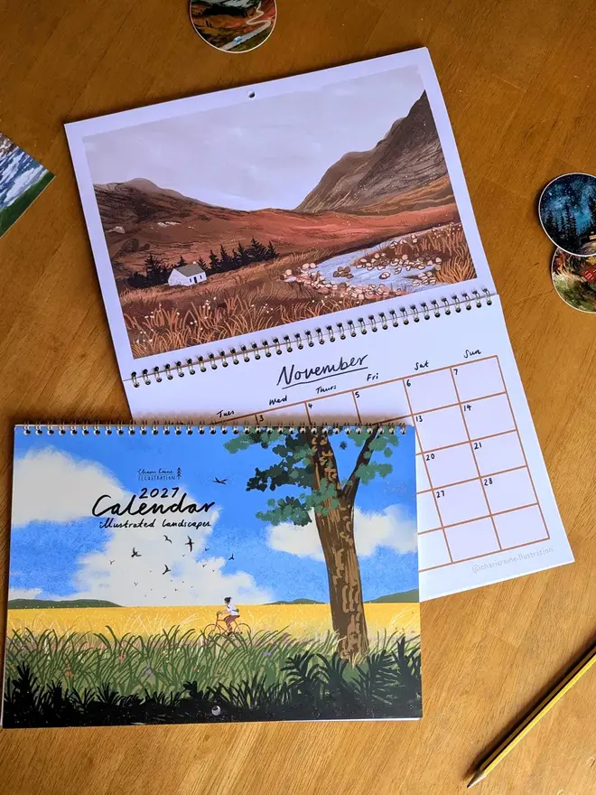 Illustrated landscape calendar by Charis Raine featuring a cyclist though yellow and green fields, with a tree and blue sky