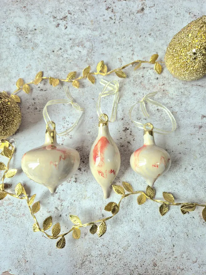 Ceramic christmas bauble decorations in a pearlescent glaze with white, cream and pink and gold, with silk ribbon and gold detailing. Photographed on a pearlescent serving dish with gold pears and christmas lights, gift, christmas, ceramics, pottery, christmas, decorations, christmas tree