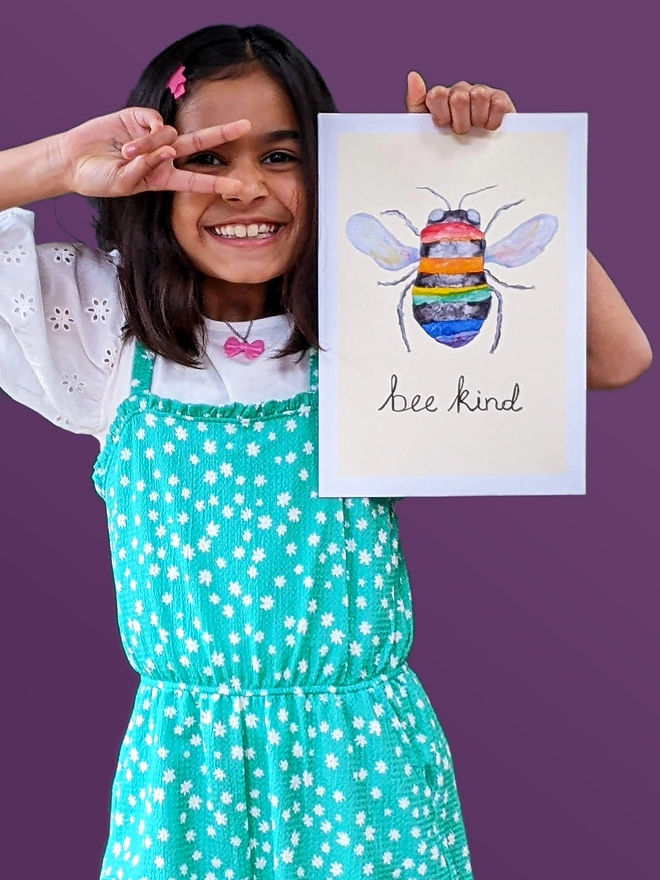 Young girl standing holding an art print saying 'Bee kind'
