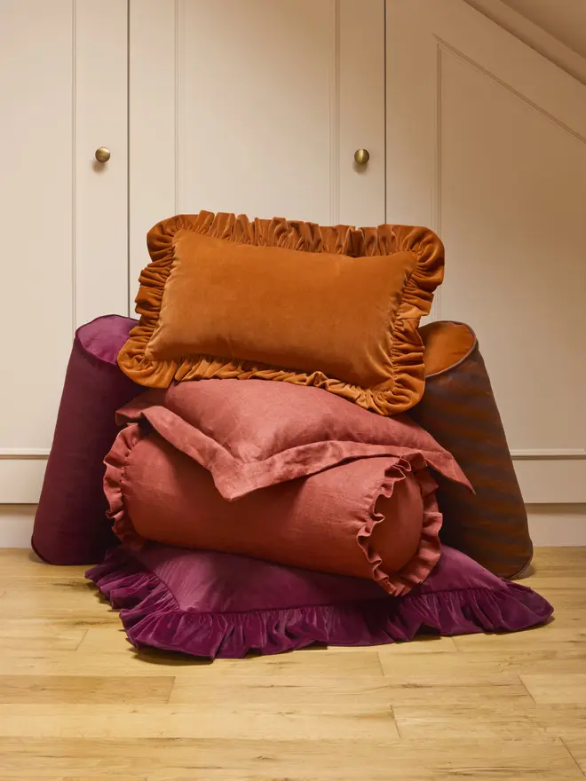 Group of velvet and linen cushions with ruffled, piped and Oxford edges, in rust and burgundy tones