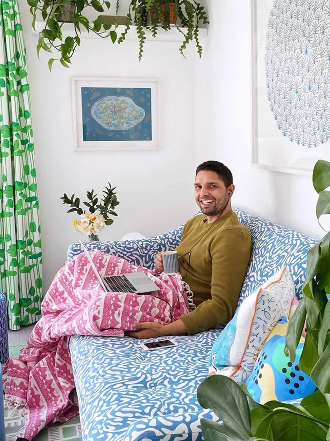 Pink Belle Mare Woven Throw, a person sitting on a blue sofa with a pink throw. 