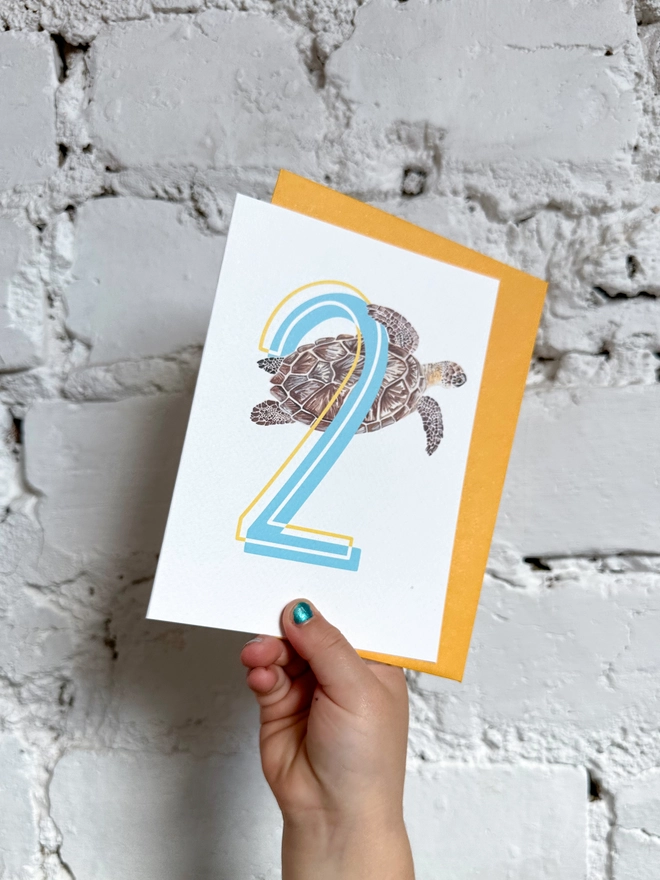 a white card with a big blue number 2 and a turtle illustration with a bright yellow envelope