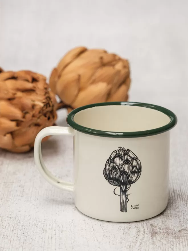 Picture of a Cream Enamel Mug with a Green Rim with an artichoke design etched onto it, taken from an original Lino Print