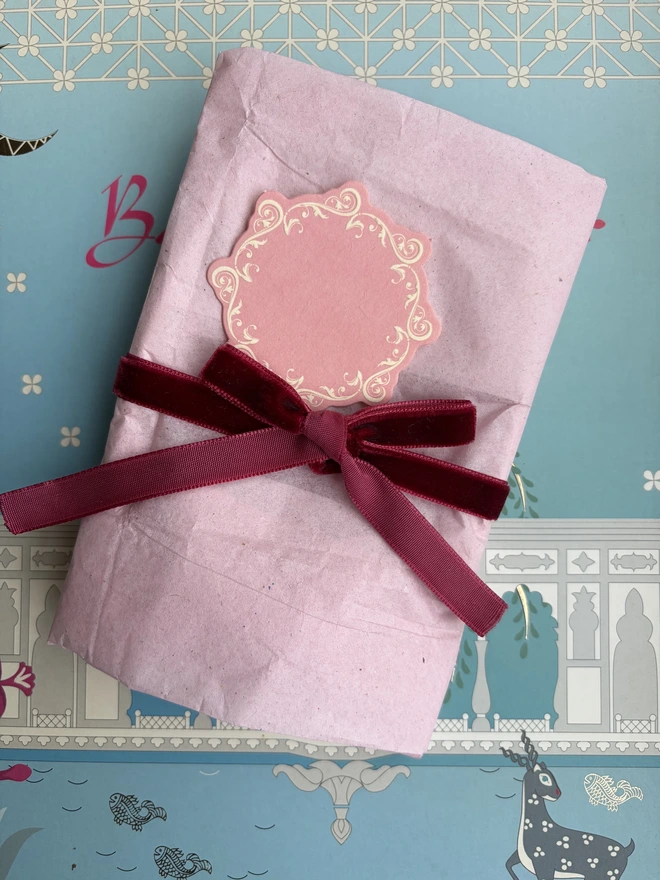 Handmade ceramic cheese platter wrapped in tissue and tied with a bow with a gift tag attached.