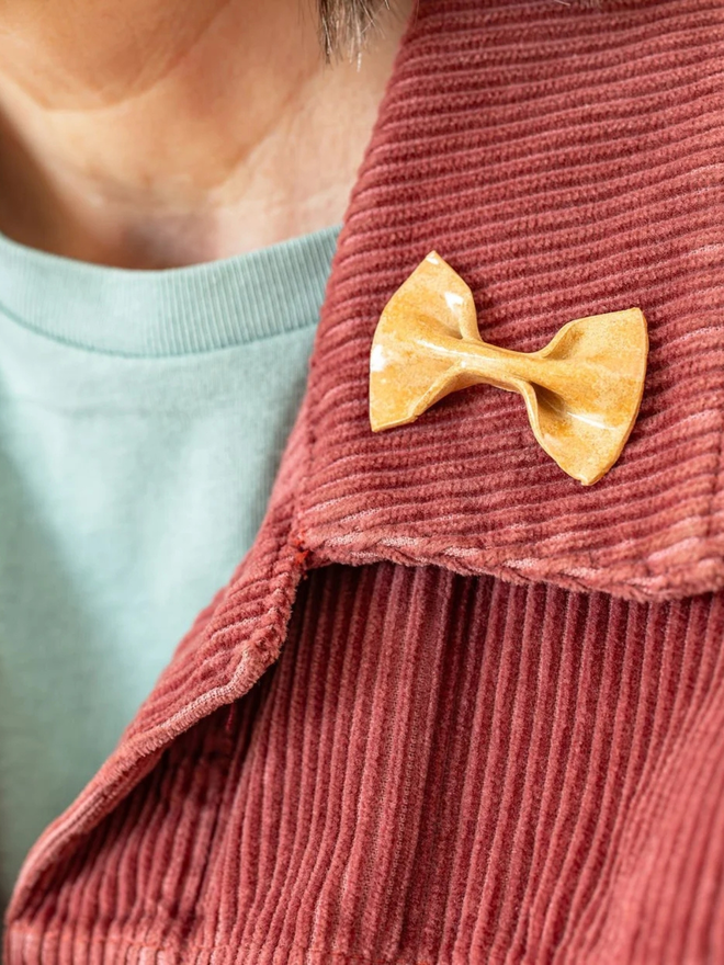 ceramic pasta pin badges. a ceramic farfalle badge photographed on a jacket.