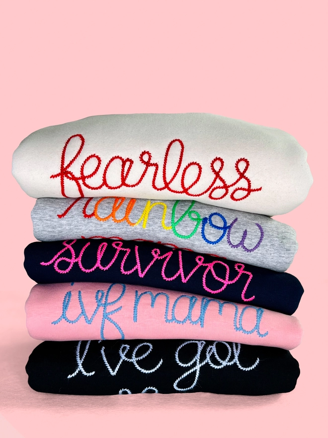 A bundle of colourful embroidered sweatshirts on a pink background