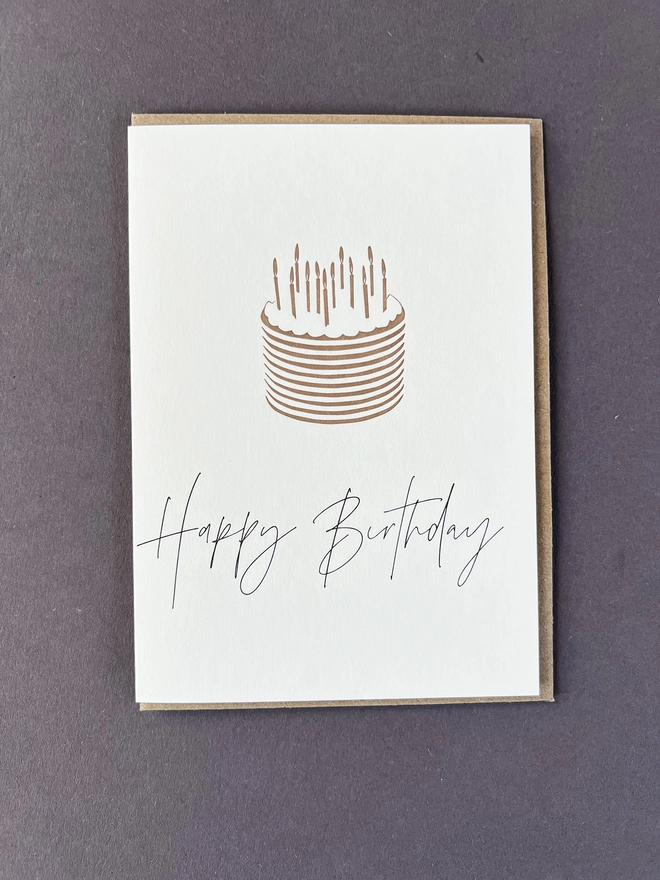 A simple Metallic gold cake with candles and 'Happy Birthday" beautifully written in modern calligraphy underneath.