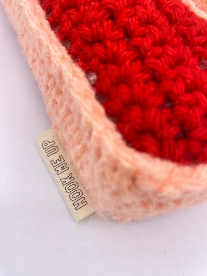 Close up of brand label on Crocheted D Cushion in Red and Peachy Pink
