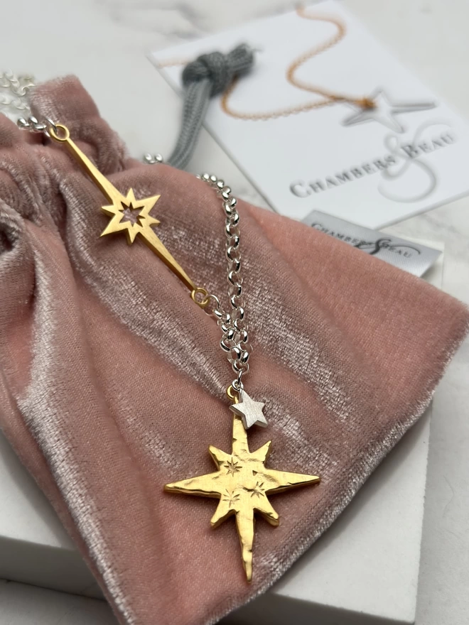 Large rough hewn gold star hanging from a sterling silver chain with a silver mini star. There is a gold interstellar charm incorporated into the silver chain.