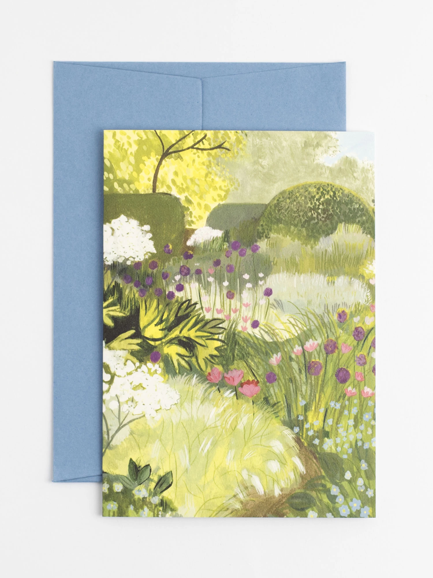 A greetings card featuring an illustration of a garden. The garden is very green and bursting with purple tulips, small bue flowers and frothy white cow parsley in the foreground.