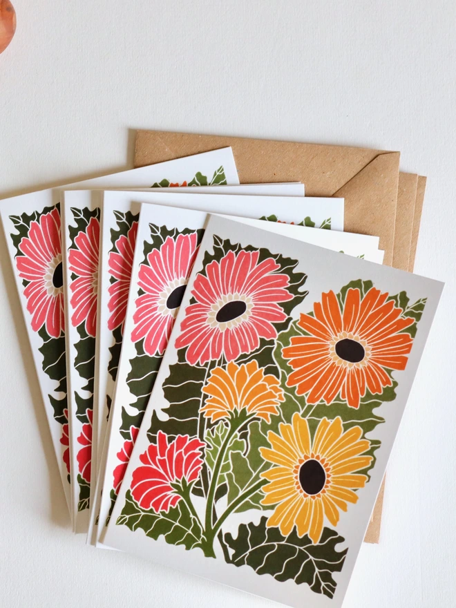 Set of 8 hand-carved botanical notecards featuring Gerbera Daisies. A6 linocut print greeting cards in colourful pink, orange and yellows, displayed with kraft envelopes. Cottagecore stationery on recycled cardstock.