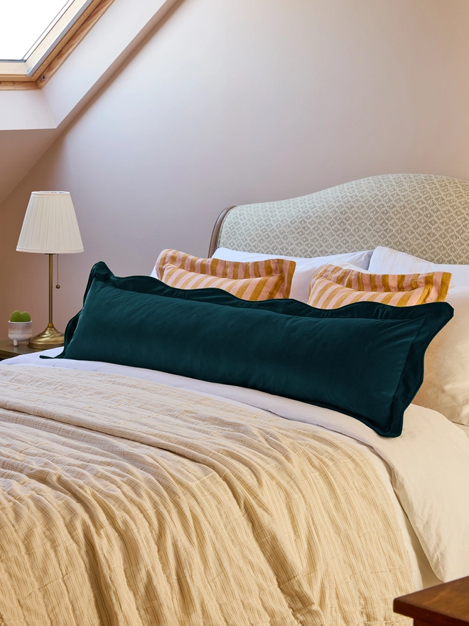 Handmade scalloped deep teal velvet bolster cushion 130cm with feather pad paired with stripe linen cushions on bed, Kika Bespoke