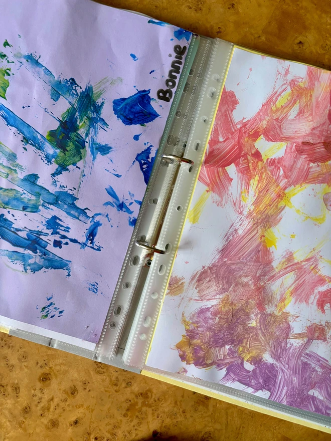 a personalised keepsake ring binder open on a desk filled with a child's nursery artwork