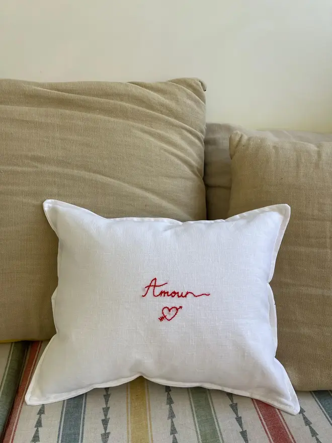 'Amour' Hand Embroidered Linen Cushion Hearth Design, white cushion on a sofa