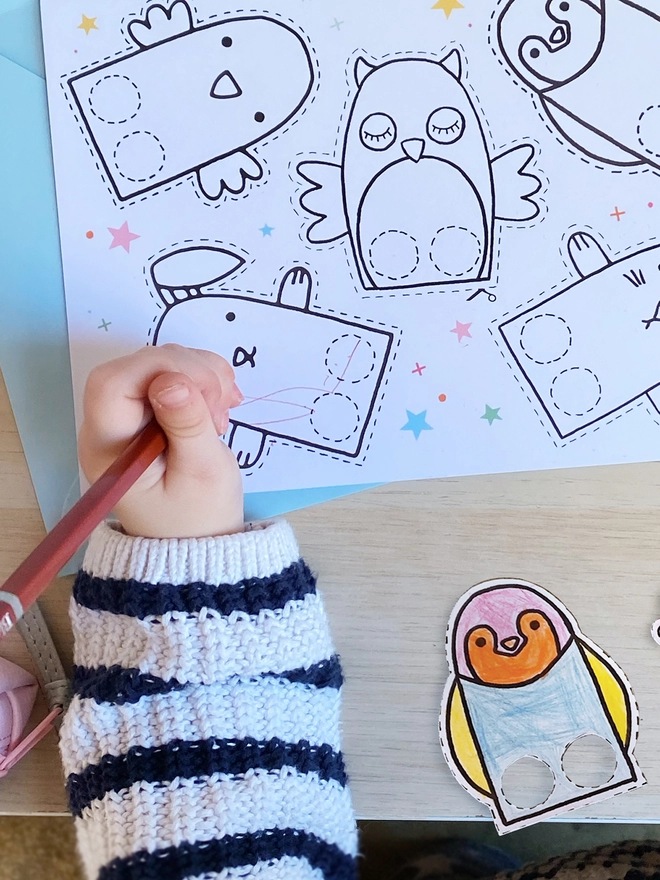 A child is colouring in finger puppets on a greetings card that has several printed on.