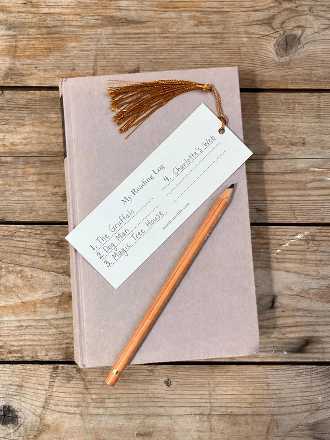 The back of a traditional card book mark showing a reading log that has been filled in by a child with a list of their favourite books the bookmark is cream with a golden brown silky tassel