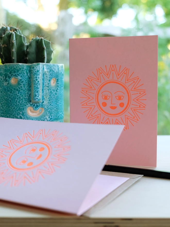 Two sunshine cards on a table with cactus plant and pencil.