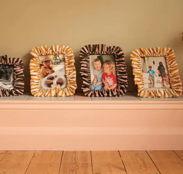 Multiple soft ruffled frames with striped fabric trim displayed on a cabinet. 