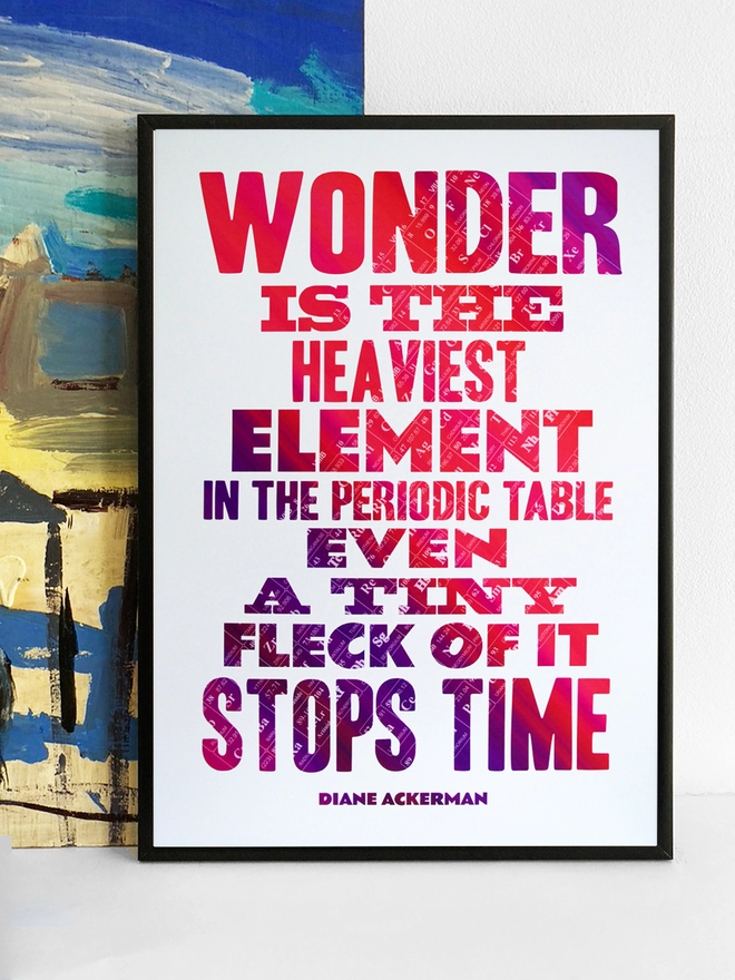 Framed multicoloured typographic print of “Wonder is the heaviest element in the periodic table, even a tiny fleck of it stops time” by Diane Ackerman.  The print rests against a blue and yellow abstract painting.