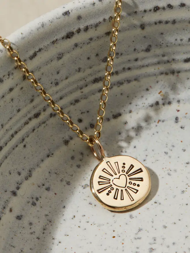 9ct Gold Darling Heart Pebble Necklace hanging over a bowl