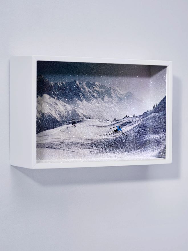 Miniature scene in an artbox showing a tiny male skiing figurine skiing against a sparkling mountainous backdrop 