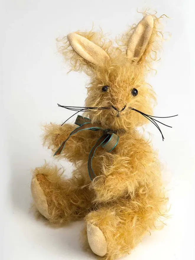 Brown stuffed rabbit sitting upright against a white background, wearing a green and blue ribbon.