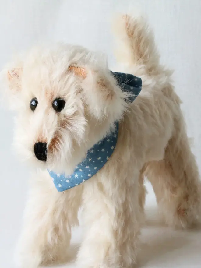 Handmade cream-colored teddy dog wearing a blue bandana standing against a plain background.
