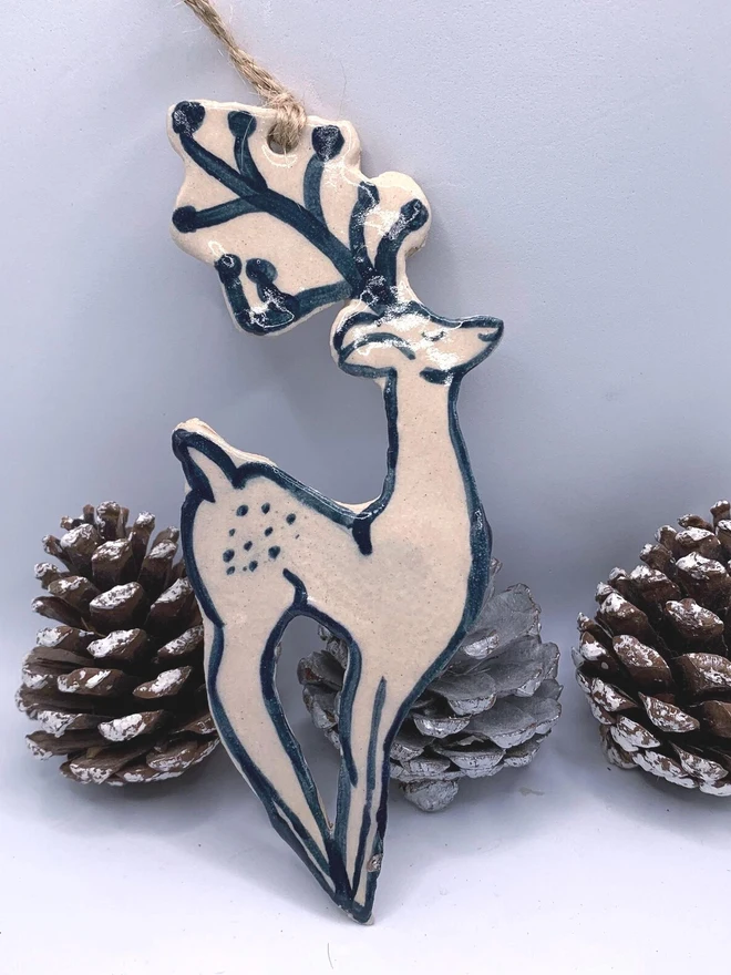 Handmade Ceramic Reindeer Ornament Scandinavian Folk Decor, a colourful reindeer decoration sitting on a plain surface joined by some acorns. 