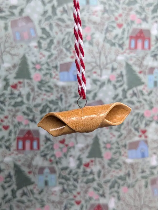 ceramic garganelli christmas decoration. a ceramic pasta decoration hanging from white and red thread.