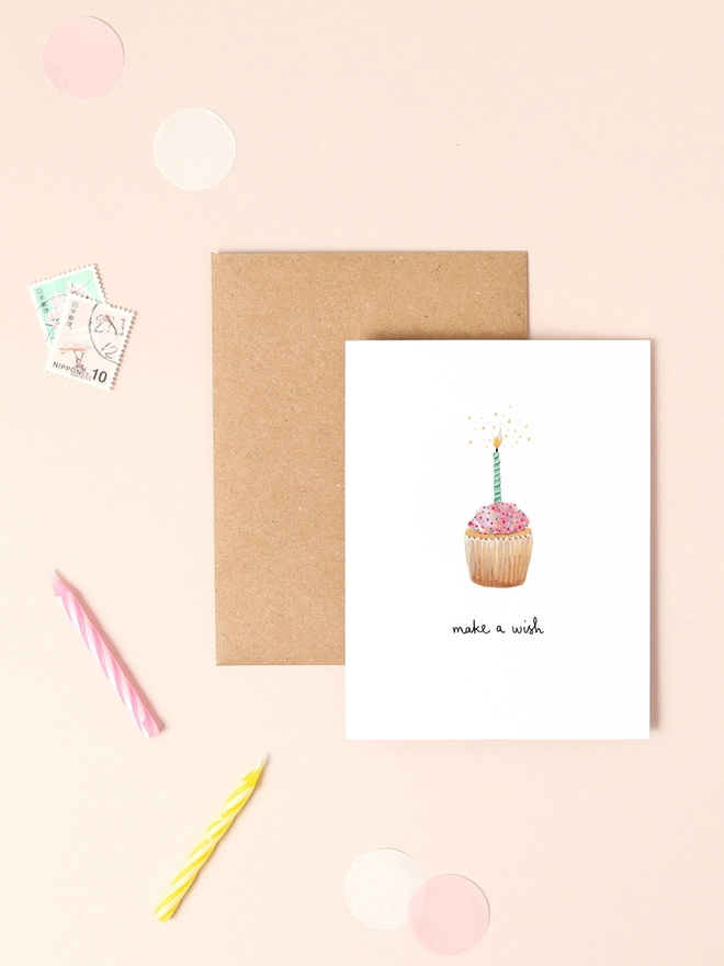 A delightful illustration of a beautifully decorated cupcake topped with colorful sprinkles and a glowing candle, accompanied by the cheerful message "Make a Wish" in a playful, handwritten font. The design features vibrant colors and a whimsical style, capturing the joy and excitement of celebrations.