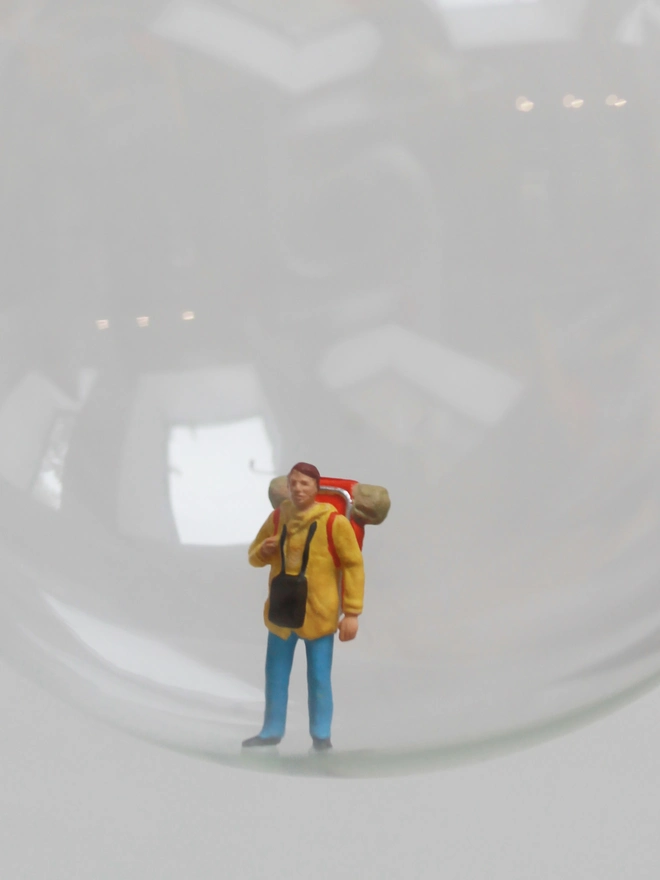 Miniature figure of a backpacker in a glass Christmas bauble - close up 