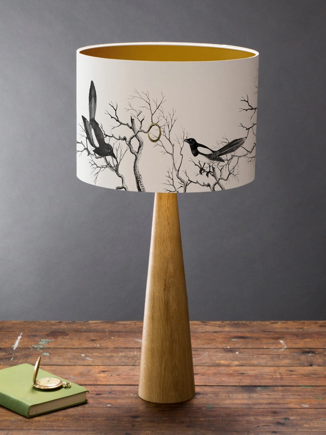 Drum Lampshade featuring magpies sitting on branches on a wooden base on a shelf with books and ornaments