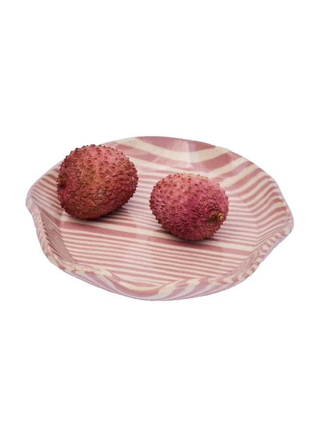 Striped Trinket Dish, a colourful trinket dish sitting on a white surface against a plain backdrop. It is accompanied by some lychees. 