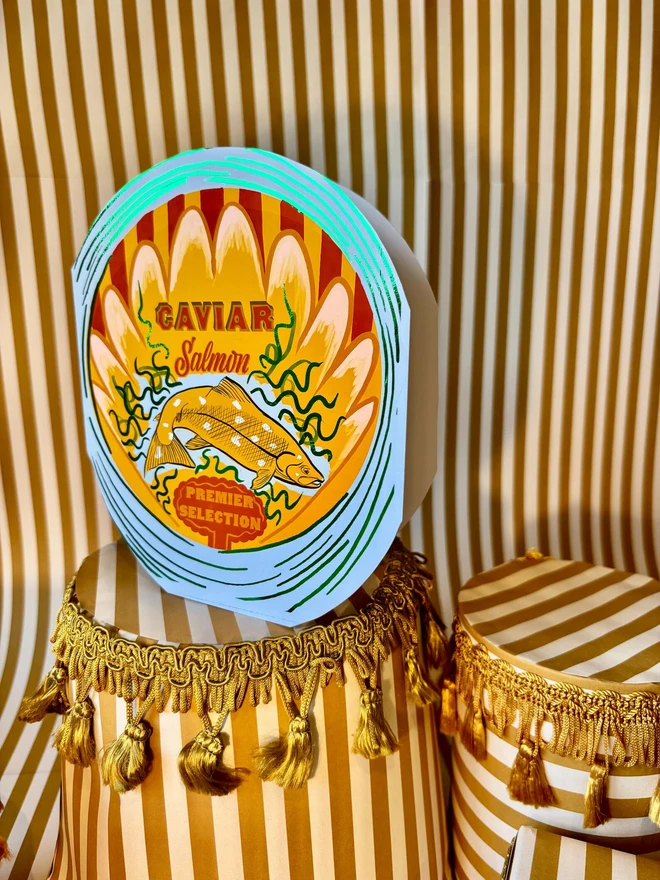 Salmon Round Tin Card, a colourful card sitting on a decorated display in front of a backdrop. 