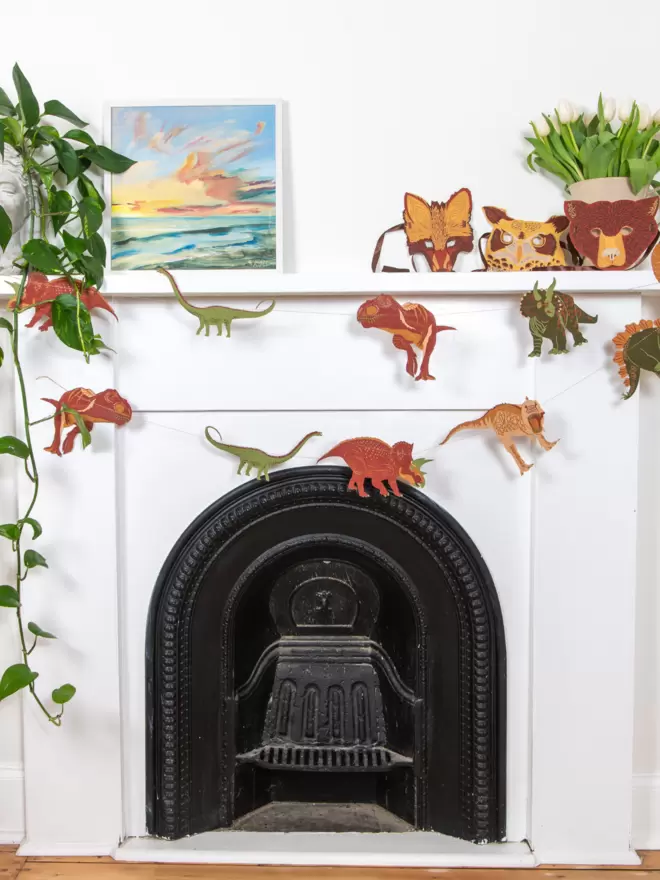 Dinosaur shapes hung on a white mantelpiece, with plants, canvas and animal face masks