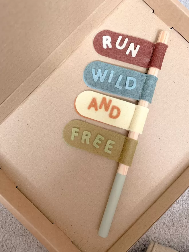 Swizzler stick in brown, blue, yellow and green. Tabs say run, wild and free. Stick placed in a box.