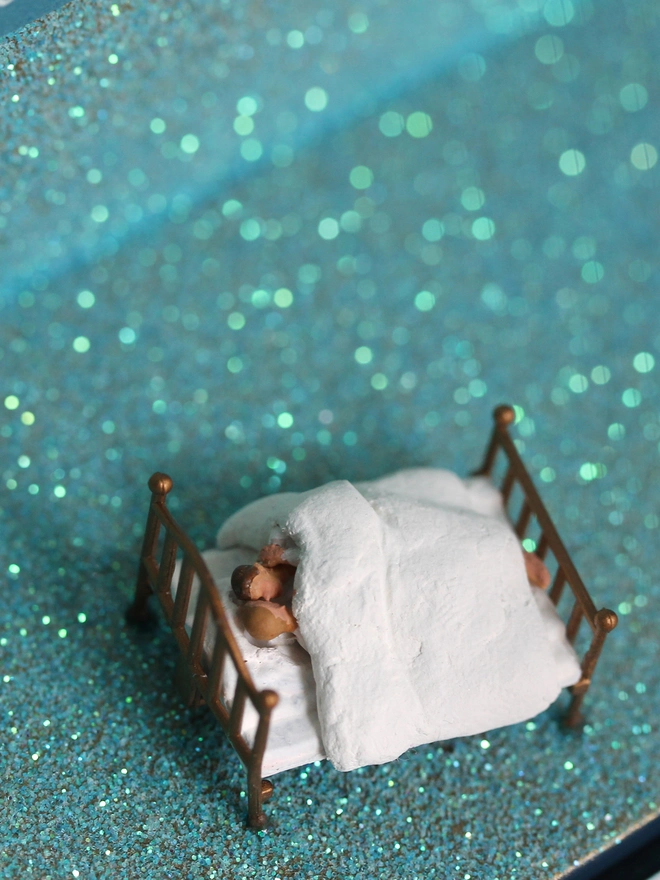 Miniature scene in an artbox showing two men lying in bed against a sparkling backdrop evoking the night sky.