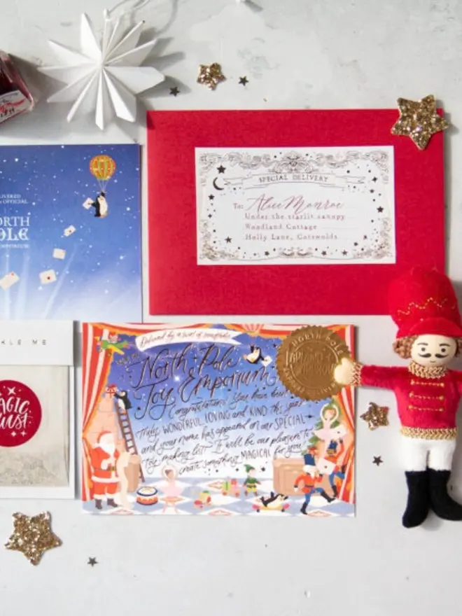 The illustrated North Pole notecard with a gold "Lapland Approved" seal, the starry blue card back, a red envelope with a personalised "Special Delivery" label and a Magic Dust bag, with a felt nutcracker holding the corner of the card.