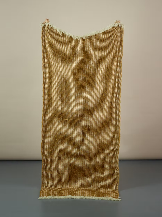 Grainne Honeycomb Lambswool Blanket. a yellow textured blanket photographed against a plain wall.