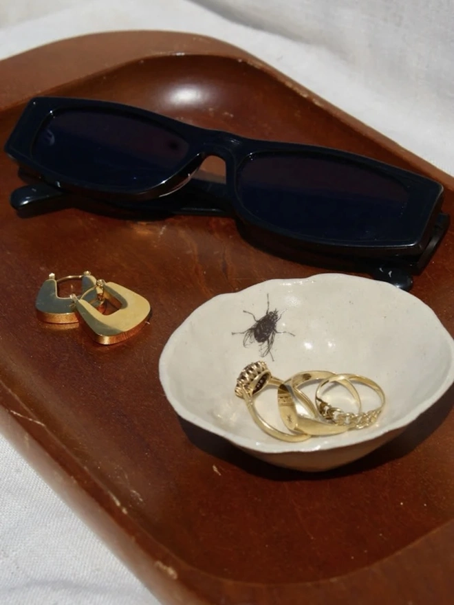 Fly Trinket Dish, a fly trinket dish sitting on a wooden surface joined by other accessories. 