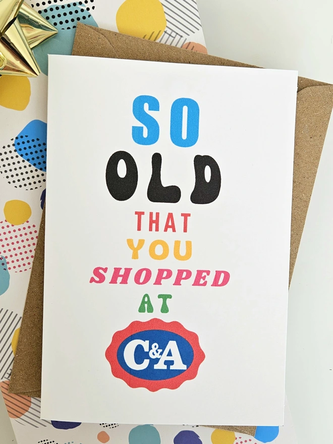 A photograph of the front of a humorous A6 greeting card illustrated using brightly coloured text and the retro shop logo. The text says so old you shopped at C&A