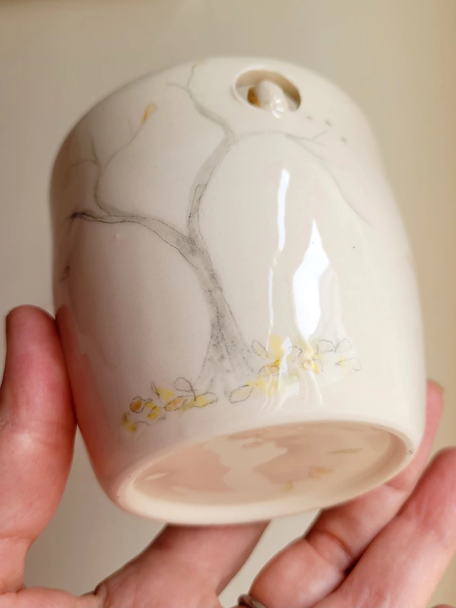 hand holding a cream ceramic mug with a painted tree with autumn leaves and an owl perched high in a cut out 