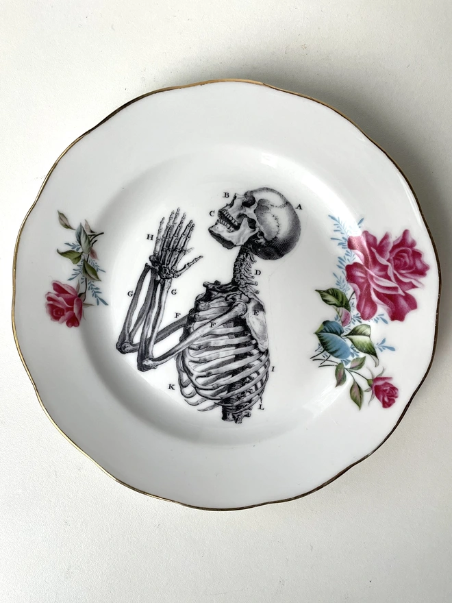 vintage plate with an ornate border, with a printed vintage illustration of a praying skeleton in the middle