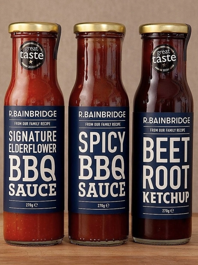 Sauce Trio (Set Of 3), a collection of 3 jars sitting on a wooden surface against a plain backdrop. 