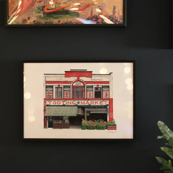 Watercolour illustration of Tooting Market, framed in black and hanging against a dark wall