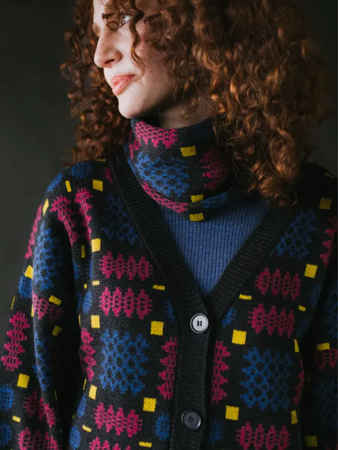 Model wearing pieces from MABLI's 'Carthen' collection, featuring the Carthen Cardigan in the vibrant 'Fireworks' colour-way. The design showcases bold, colourful patterns inspired by traditional Welsh blanket tapestry.