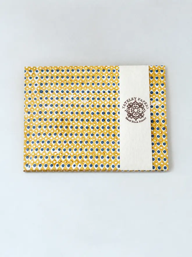 A4 Large Landscape Travel Watercolour Book. A hand block printed Yateley Papers item covered in mustard yellow diamond lattice paper with navy blue dots, wrapped in a cream branded paper band. The textured printed cover gives a handmade, artisan look suited to gifting or stationery.