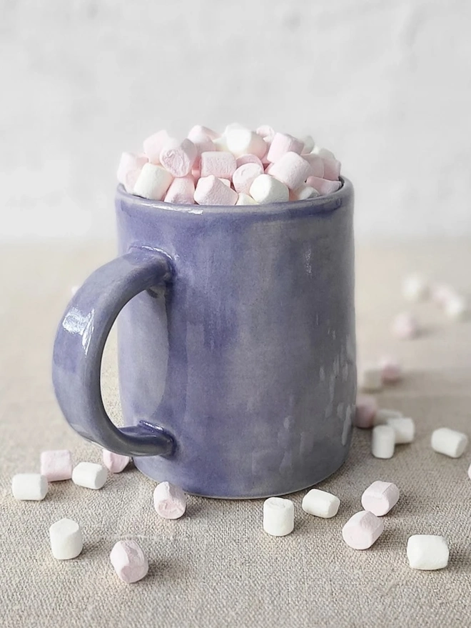 Ceramic Pint Mug, a colourful ceramic mug sitting on a plain surface against a white backdrop. It is accompanied by some marshmallows. 